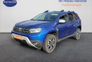 Dacia Duster bleu Iron en 3/4 avant droit avec jantes bi-ton et barres de toit visibles.
