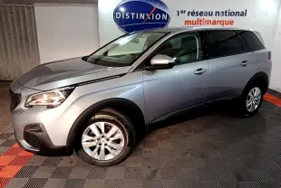 Peugeot 5008 gris clair vue 3/4 avant droit en intérieur, avec jantes alliage et feux allumés.
