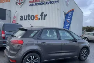 Vue côté gauche arrière d'une Citroën C4 Picasso marron avec jantes alu, stationnée devant un garage autos.fr par temps couvert.