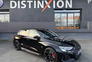 Audi RS3 Sportback noir vue 3/4 avant droit avec jantes noires et étriers de frein rouges devant un mur gris.
