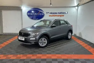 Volkswagen T-Roc gris foncé vue 3/4 avant droit dans un showroom avec sol noir et bandes orange.