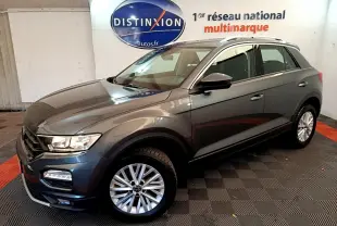 Volkswagen T-Roc gris foncé vue 3/4 avant droit, avec jantes alliage et barres de toit argentées.