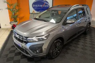 Vue 3/4 avant droit d’un Dacia Jogger gris schiste métal 2025 avec barres de toit et jantes noires en showroom.