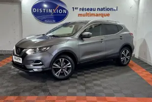 Nissan Qashqai gris foncé en 3/4 avant droit, avec jantes alliage et feux LED, dans un showroom intérieur.