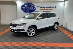 Vue 3/4 avant droite d'un Skoda Karoq blanc stationné en intérieur sur sol noir et orange avec logo Distinxion en arrière-plan.