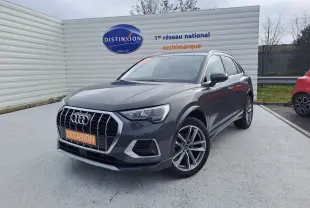 Audi Q3 gris nano en 3/4 avant droit, avec jantes alu 19 pouces et calandre chromée visible sur parking extérieur.