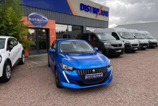 Peugeot 208 bleu en 3/4 avant stationnée devant un concessionnaire avec plusieurs véhicules utilitaires en arrière-plan.
