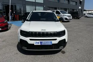 Vue avant d’un Jeep Avenger blanc électrique 2025 avec calandre noire et plaque « Véhicules Occasions » sur parking.