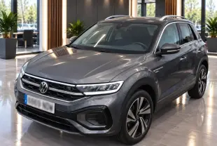 Volkswagen T-Roc gris platinium en vue 3/4 avant droit, avec calandre R-Line et jantes alliage distinctives.