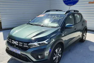 Vue 3/4 avant droite d'une Dacia Sandero Stepway 2025 vert cèdre avec barres de toit et calandre noire distinctive.