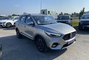 MG ZS gris foncé vu en 3/4 avant droit sur un parking ensoleillé avec calandre noire distinctive.