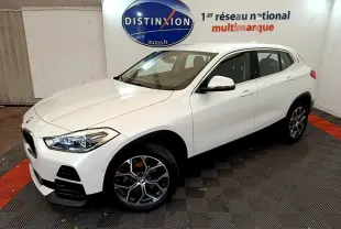 BMW X2 blanc en 3/4 avant droit dans un showroom avec jantes alliage et phares LED allumés.