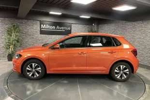 Volkswagen Polo orange vue de profil côté gauche, avec jantes alliage et intérieur visible en showroom.