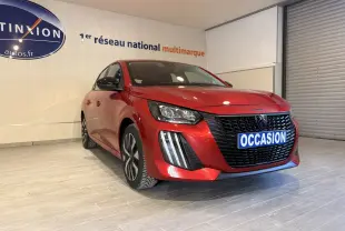 Peugeot 208 rouge vue 3/4 avant droit en intérieur, avec calandre noire et plaque "OCCASION" visible.