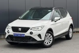 Vue 3/4 avant droite d'un SEAT Arona blanc avec toit noir et jantes alliage, stationné devant un mur gris.