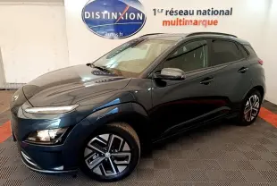 Hyundai Kona électrique bleu en 3/4 avant droit, avec jantes alliage et rétroviseurs chromés dans un showroom.