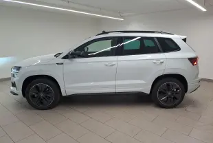 Vue de profil côté gauche d'un Skoda Karoq blanc lune 2025 avec jantes noires et toit ouvrant dans un showroom.