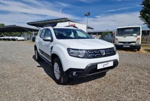 Dacia Duster 4x4 blanc en 3/4 avant droit sur parking extérieur, avec calandre noire et jantes alliage 16 pouces.