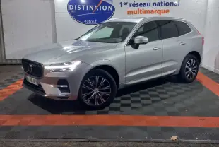 Volvo XC60 gris clair en 3/4 avant droit, stationné en intérieur sur sol damier noir et orange.