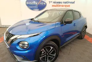 Nissan Juke bleu en 3/4 avant droit, avec toit noir et jantes alliage distinctives, en intérieur showroom.