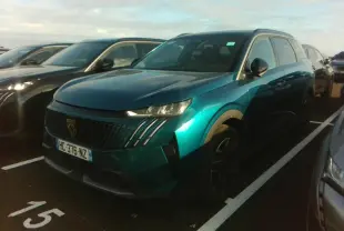 Peugeot 5008 bleu foncé vue 3/4 avant droit sur parking, calandre noire avec griffes LED distinctives.