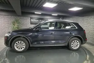 Audi Q5 bleu métallisé vue de profil côté gauche dans un showroom avec jantes 17 pouces et sellerie claire visible.