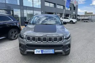 Vue de face d'un Jeep Compass gris 2023 avec capot noir mat et calandre distinctive en sept fentes, stationné devant un concessionnaire.