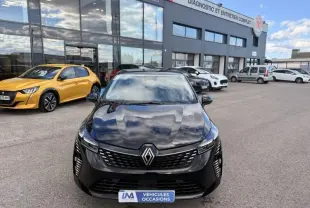Vue avant d'une Renault Clio V noire 2025 avec calandre moderne et logo Renault bien visible, stationnée devant un garage.