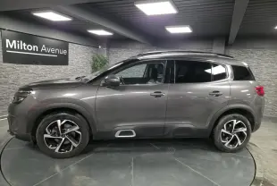 Vue profil côté gauche d'un Citroën C5 Aircross gris métallisé avec jantes alliage et barres de toit noires.