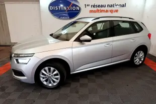 SKODA KAMIQ gris clair vu de profil côté gauche, intérieur showroom avec logo Distinxion en arrière-plan.