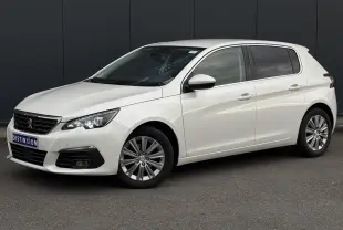 Peugeot 308 blanc nacré vue 3/4 avant droit, avec jantes alliage et projecteurs LED allumés.