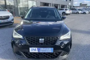 Vue de face d'un SEAT Arona noir 2023 avec calandre hexagonale et phares LED allumés sur parking extérieur.
