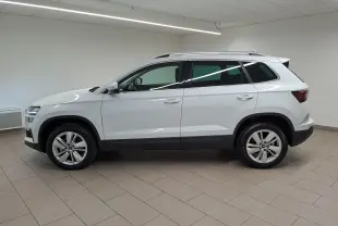 Vue de profil côté gauche d’un Skoda Karoq blanc lune 2025 avec jantes alliage et toit ouvrant en intérieur neutre.