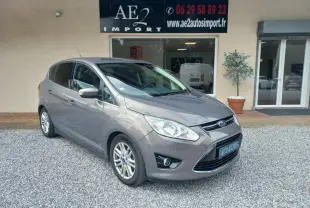 Ford C-MAX gris en 3/4 avant droit, avec calandre chromée et jantes alliage, stationné devant un commerce.