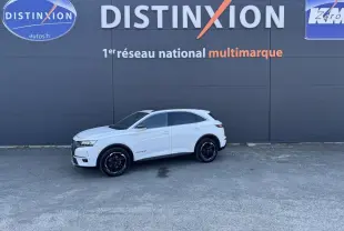 Vue de profil droit d'un DS7 Crossback blanc stationné devant un mur gris avec logo Distinxion.