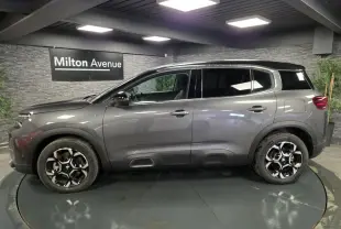 Profil côté gauche du Citroën C5 Aircross Hybrid gris avec toit noir et jantes alliage bi-ton dans un showroom.