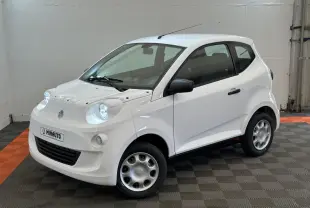 Vue 3/4 avant d'une Aixam Minauto E Access blanche avec rétroviseur caméra côté gauche dans un intérieur neutre.