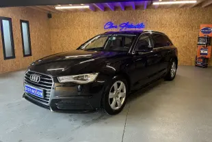 Audi A6 Avant noire vue en 3/4 avant droit dans un showroom avec éclairage intérieur et mur en bois.