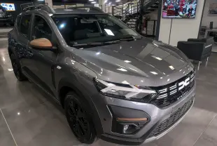 Vue 3/4 avant droite d'une Dacia Sandero Stepway TCe 110 gris schiste avec rétroviseurs bronze et jantes noires en showroom.