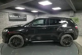 Profil côté gauche d'un Jeep Compass noir brillant avec jantes alliage noires dans un showroom intérieur.