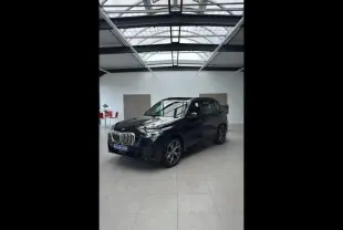 BMW X5 xDrive50e noir en 3/4 avant droit dans un showroom lumineux avec jantes alliage et calandre chromée.