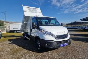 Vue 3/4 avant droite d’un Iveco Daily blanc avec benne relevée et coffre latéral sous un ciel bleu.