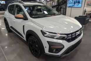 Vue 3/4 avant droite d'une Dacia Sandero Stepway 2025 blanc glacier avec rétroviseurs bronze et jantes noires en showroom.