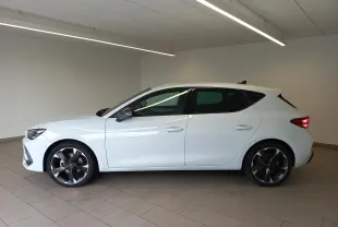 Vue de profil côté gauche d'une CUPRA Leon blanche Nevada avec jantes noires et détails cuivrés, en intérieur.