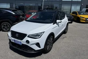 SEAT Arona blanc vue 3/4 avant droit, avec toit noir et jantes alliage, stationné devant un bâtiment vitré.