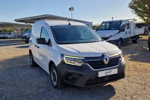 Renault Kangoo blanc en 3/4 avant droit, avec calandre noire et phares allumés sur parking extérieur.