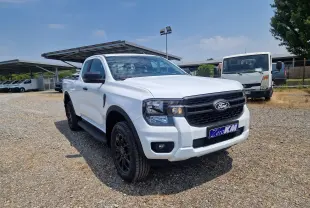 Ford Ranger Super Cabine blanc en 3/4 avant droit, avec jantes noires et marchepieds visibles sur un sol gravillonné.