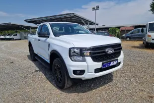 Ford Ranger Super Cabine blanc vu en 3/4 avant droit, avec calandre noire et roues noires sur terrain gravillonné.