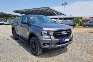 Ford Ranger Super Cabine gris carbone vu en 3/4 avant droit, avec marchepieds et barres sur le plateau.