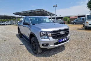 Ford Ranger Super Cabine gris Iconic vu en 3/4 avant droit, avec calandre noire et jantes noires sur parking extérieur.